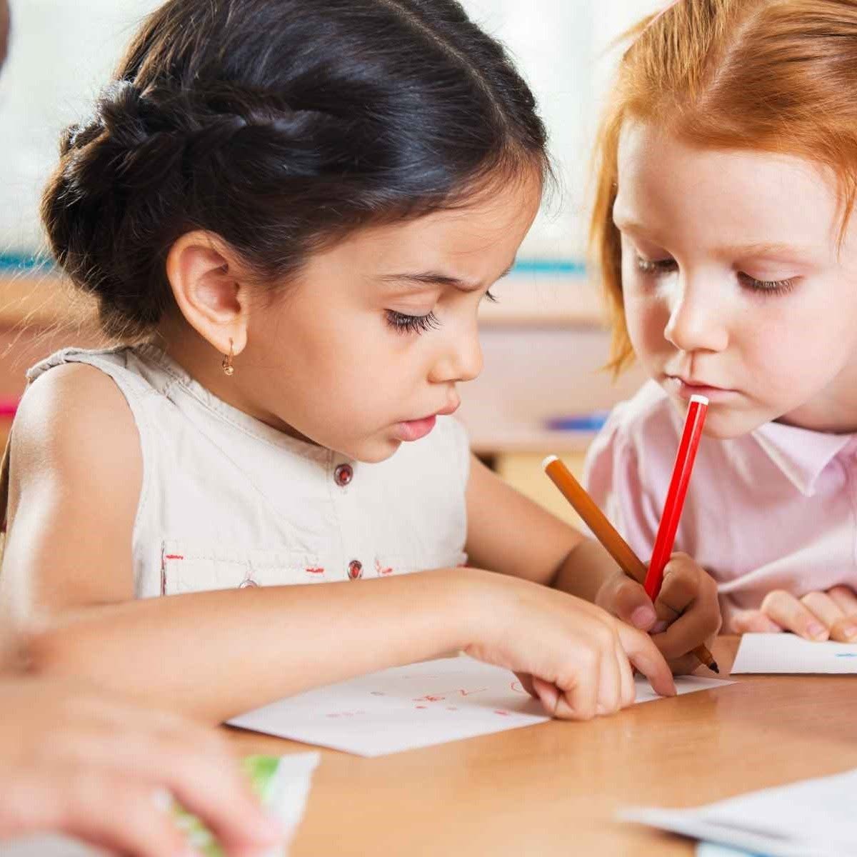 Two young girls focused on drawing together with colored pencils at a table.