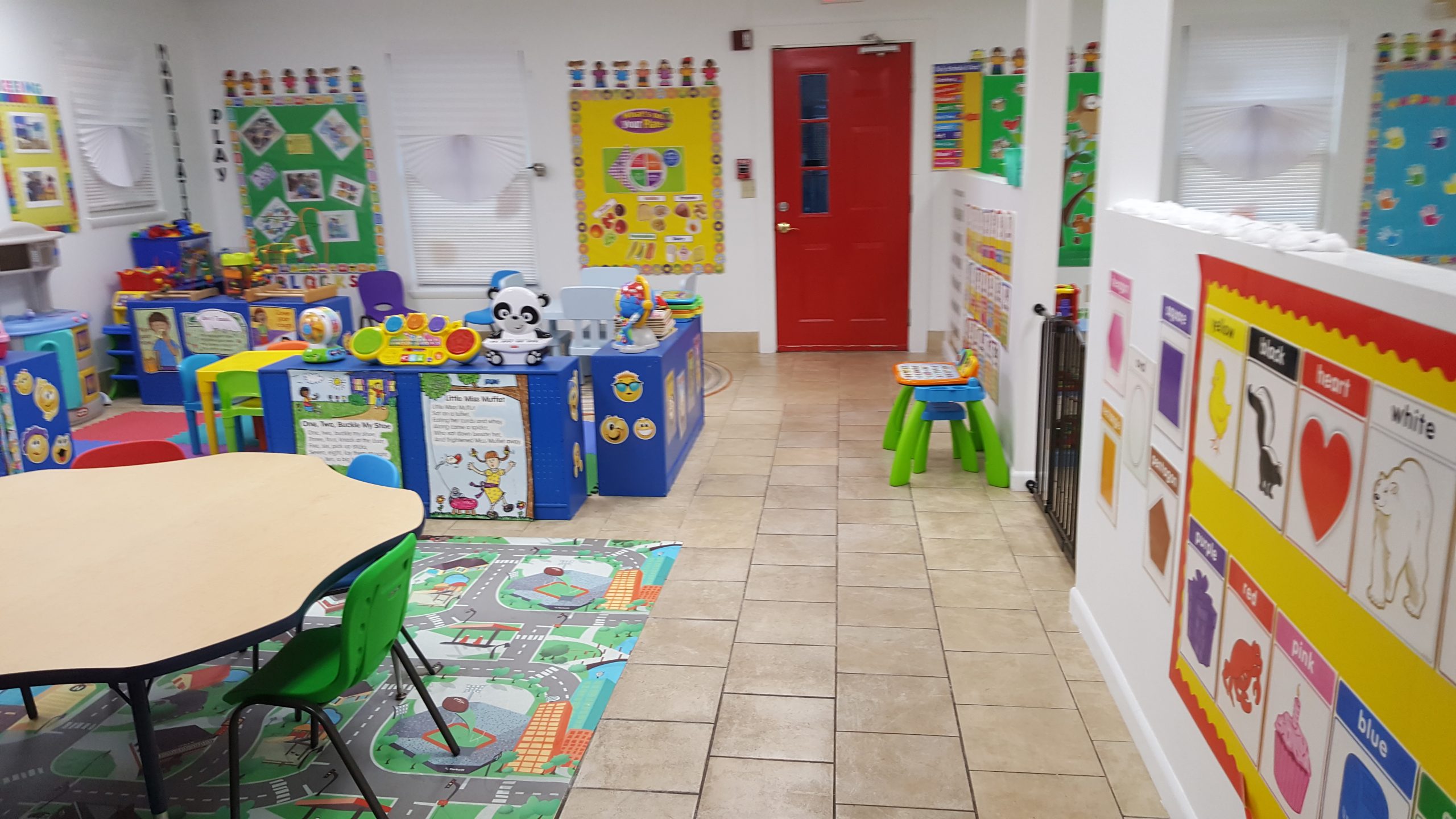 A bright preschool classroom featuring educational posters, children's tables, and colorful rugs.
