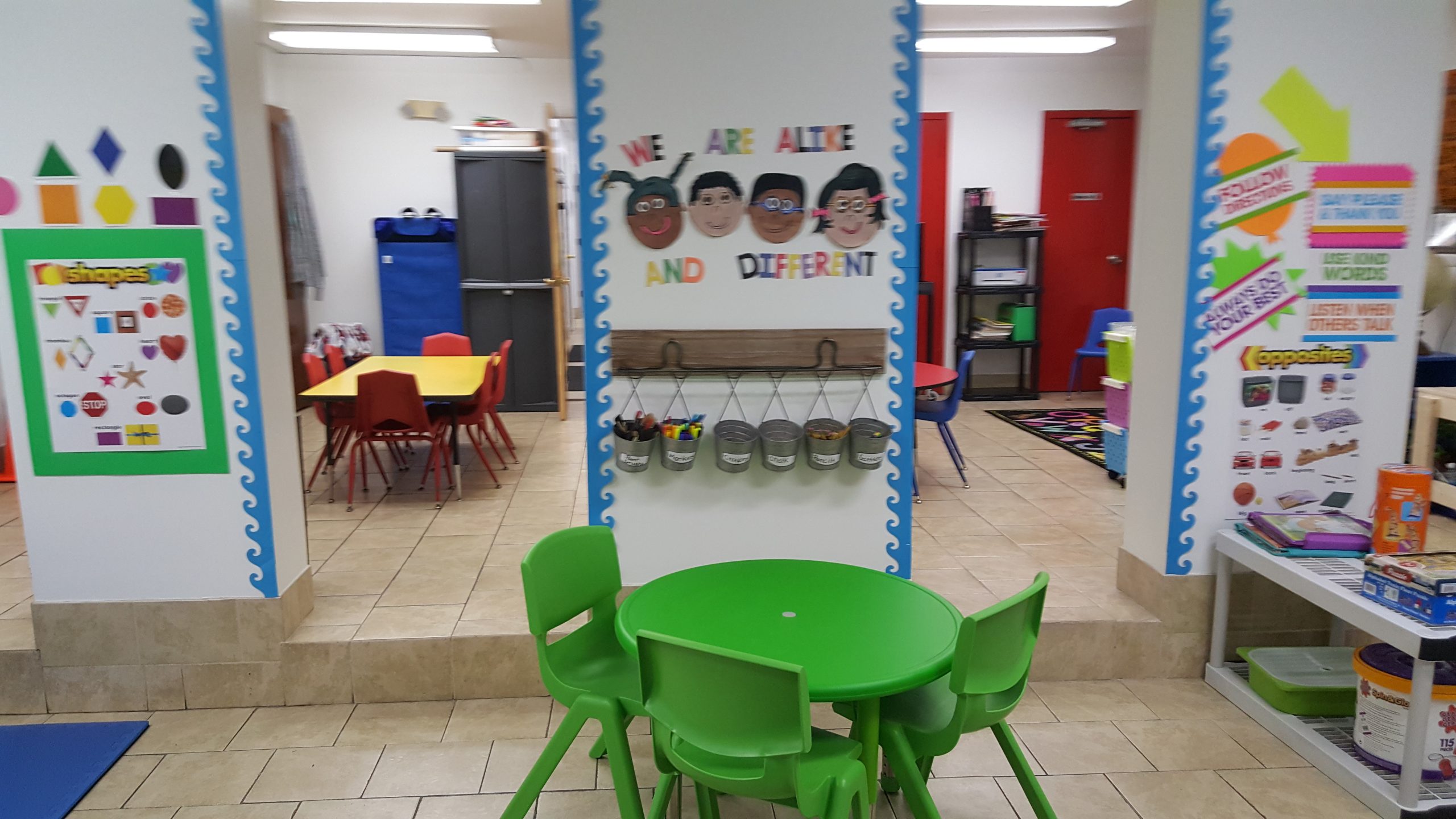 A preschool classroom featuring small green tables, chairs, and educational wall decorations for children.