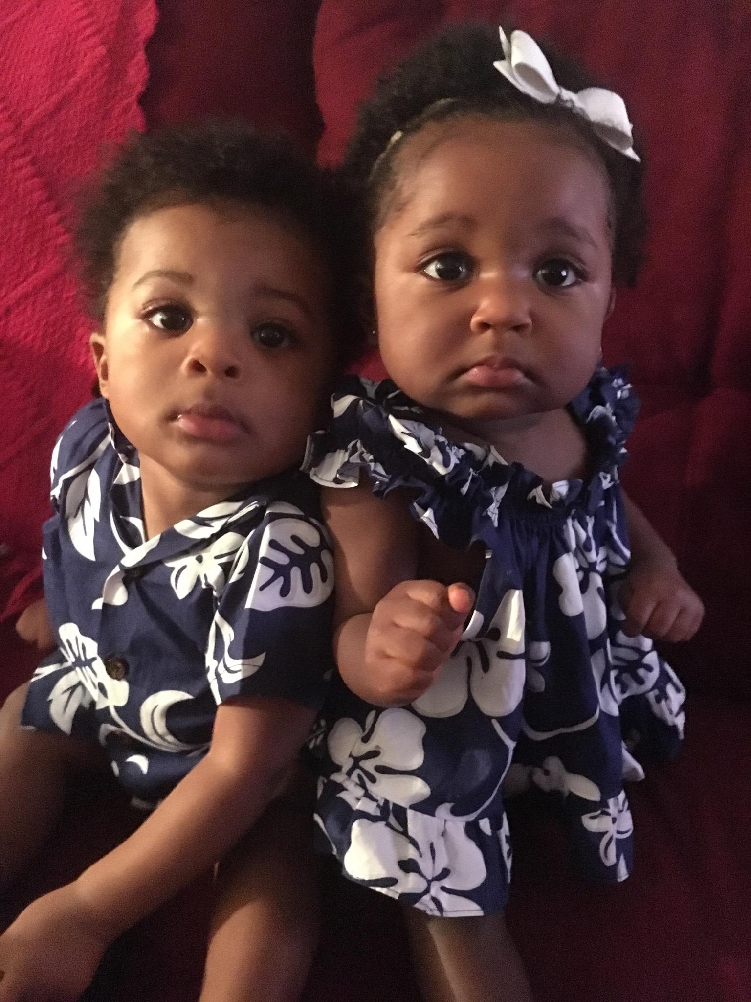 A young boy and girl sitting together wearing matching navy blue floral outfits.